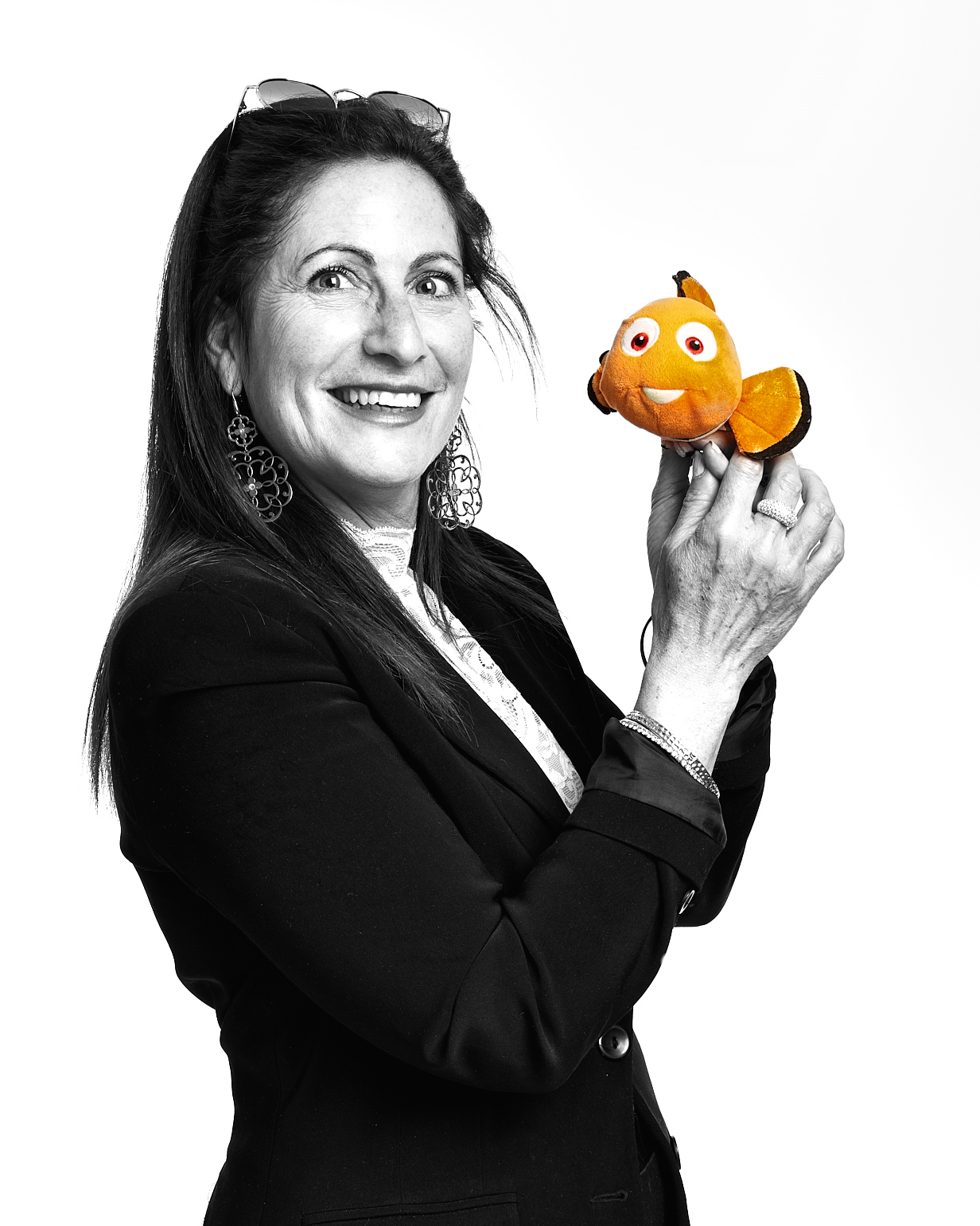 Femme souriante en noir et blanc tenant un petit poisson clown orange en peluche.