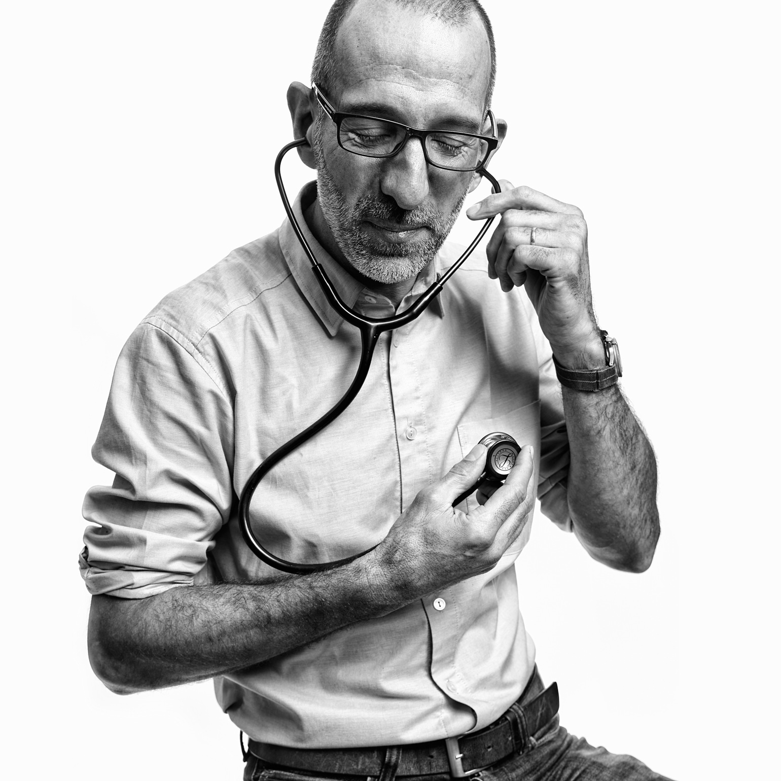 Médecin en blouse blanche, lunettes et stéthoscope, tenant un dispositif médical, regard concentré sur fond blanc.