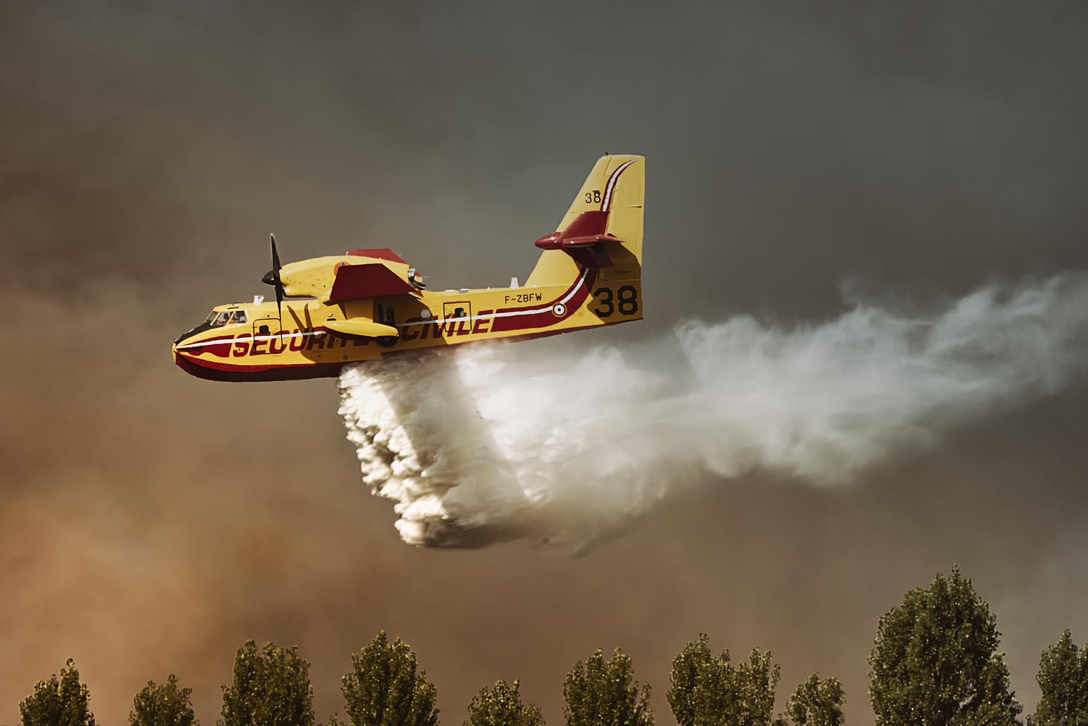 Canadair numéro 38, larguant de l’eau au-dessus d’un paysage brumeux.